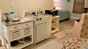 Une chambre d’hôtel de taille réduite, équipée d’une kitchenette, d’un lit, d’une chaise et d’une petite table.