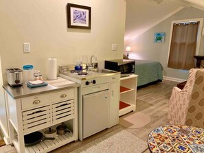 Ein kompaktes Hotelzimmer mit Küchenzeile, einem Bett, einem Stuhl und einem kleinen Tisch.