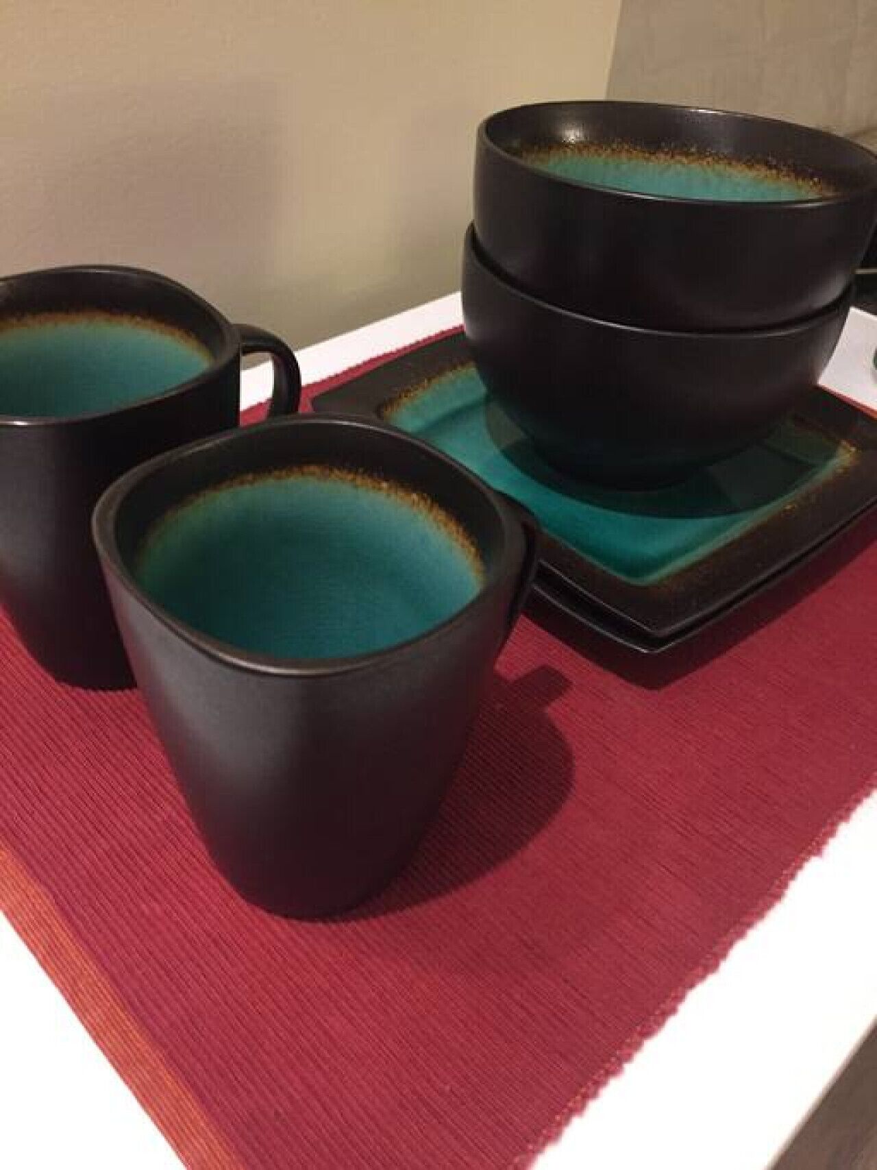 Three black ceramic cups with teal interior, placed on a red mat.