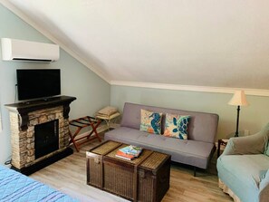 Ein gemütliches Wohnzimmer mit Kamin aus Stein, einem Flachbildfernseher, einem grauen Sofa und einem kleinen Couchtisch.