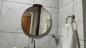 Casa de banho com um espelho redondo, uma pia preta, um porta-toalhas e azulejos de mármore branco.