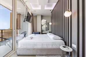 A modern hotel room with a large bed, a TV mounted on the wall, a balcony with a chair, and a round table with a remote control.