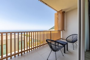 Un balcon avec vue sur la mer, deux chaises et une table.