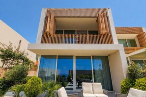 Un bâtiment moderne à deux étages, doté d’un balcon, de grandes fenêtres et d’un espace extérieur aménagé pour s’asseoir.