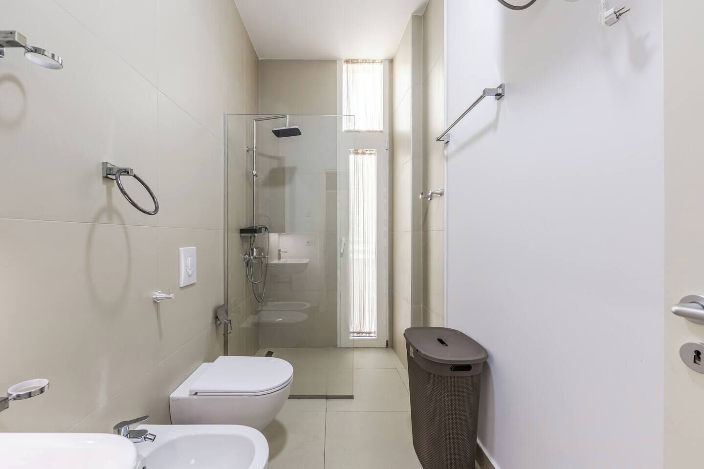 A modern bathroom with a glass-enclosed shower, a toilet, a sink, and a trash bin.