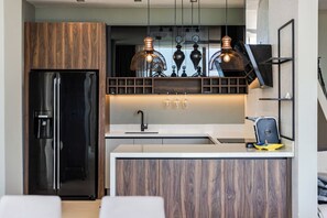 Une cuisine moderne avec un réfrigérateur noir, des armoires en bois, un plan de travail blanc et des luminaires suspendus.