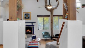 Un salon spacieux doté d’une cheminée, d’un ventilateur de plafond et offrant une vue sur l’extérieur grâce à une fenêtre.