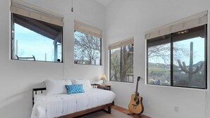 Une chambre à coucher avec un lit, une guitare et de grandes fenêtres équipées de stores.