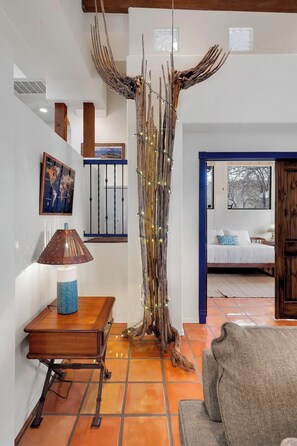 A living room with a large tree sculpture, a lamp, a map, and a bed.