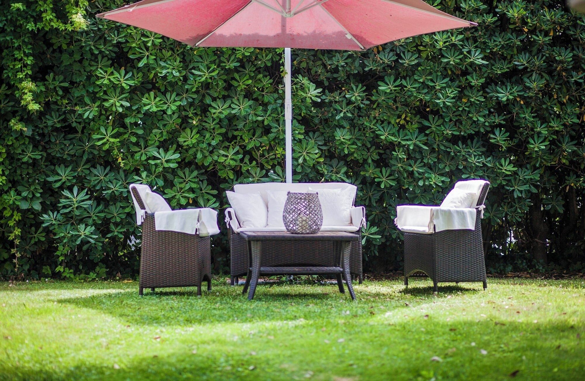 Eine Terrasse mit einer Rattan-Sitzgruppe, zwei Stühlen und einem roten Sonnenschirm.