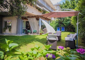 A covered outdoor seating area with wicker furniture, a pergola, and a view of a building with a balcony. - Hotel Domus (Massa)