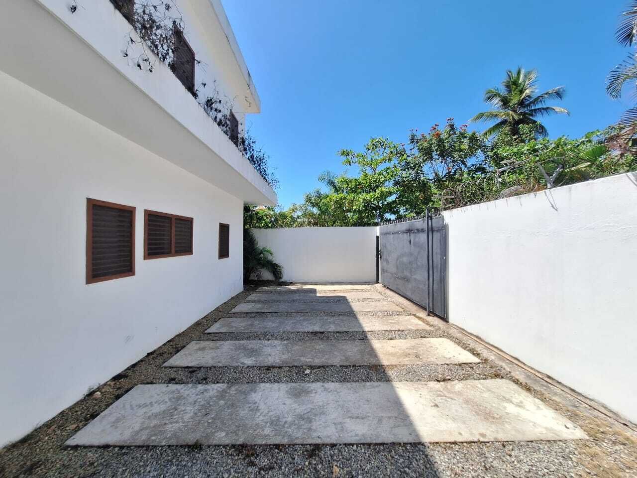 A narrow pathway leading to a building with white walls and a concrete floor.
