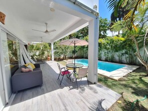 Ein überdachter Außenbereich mit Pool, Sitzgelegenheit inklusive Tisch und Stühlen, sowie Deckenventilator.
