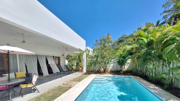 Una piscina con una casa blanca al fondo, rodeada de vegetación.