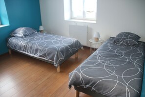 Ein Schlafzimmer mit zwei Betten, einem Fenster, einem Heizkörper und einem Nachttisch mit einer Lampe.
