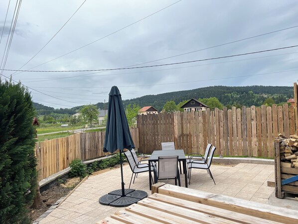 Eine Außenpatio mit Tisch und Stühlen, ein Holzzaun und Blick auf eine hügelige Landschaft.