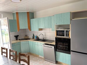 Eine Küche mit türkisfarbenen Schränken, einem Edelstahl-Geschirrspüler, einem schwarzen Backofen und einer Mikrowelle auf einem Regal.