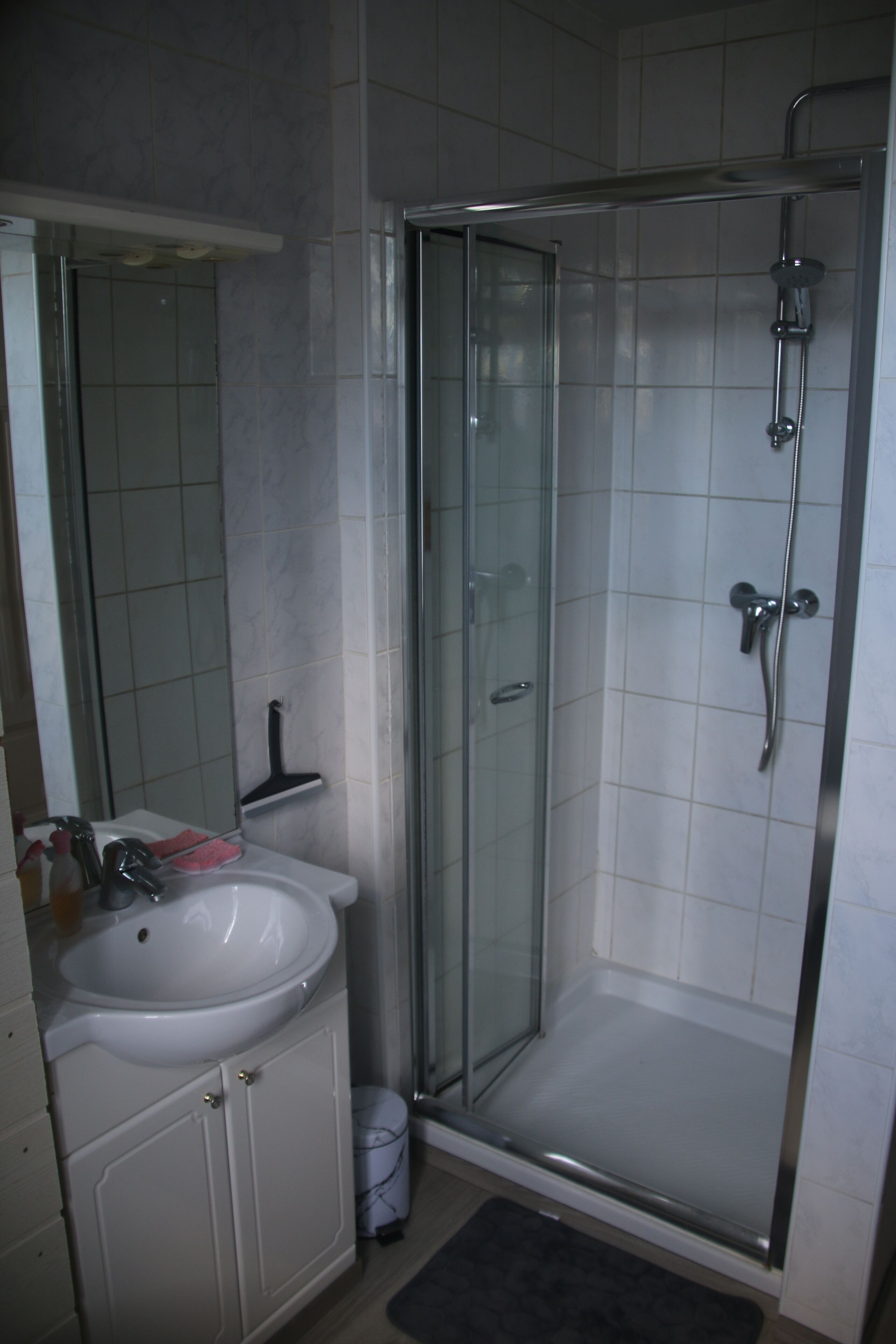 Ein Badezimmer mit einer Glaskabine zur Dusche, einem weißen Waschbecken und einem Spiegel.