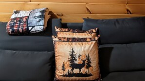 A cabin interior with a wooden wall, a sofa with decorative pillows, and three wooden signs with cabin-related phrases. - Gorgeous tiny home with mountain views in peaceful Candler (Candler)