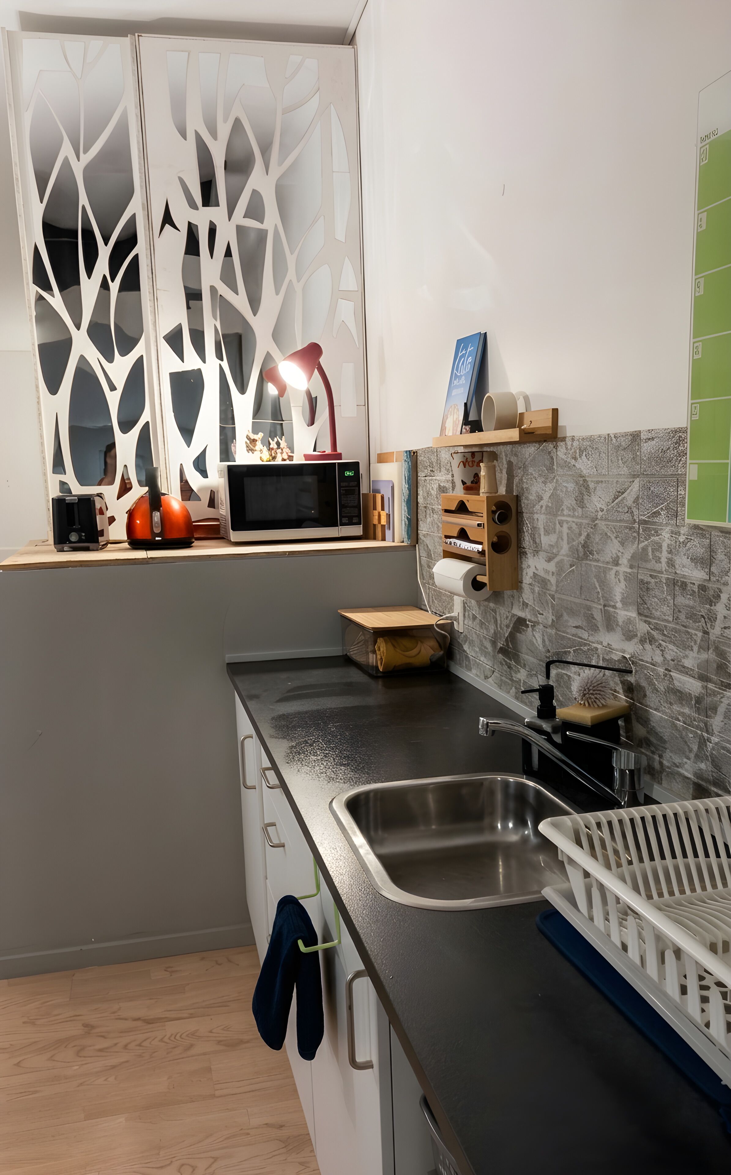 Una cocina moderna con microondas integrado, un lavamanos y una ventana con paneles blancos decorativos.