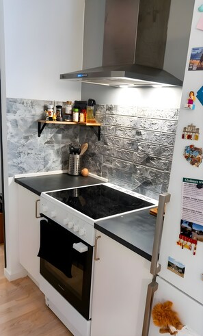 Une cuisine équipée d’une cuisinière, d’un four et d’un four à micro-ondes. On y trouve des étagères remplies d’ustensiles de cuisine et un réfrigérateur décoré d’aimants.