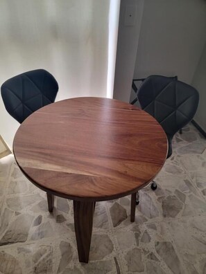 Een ronde houten tafel met vier stoelen, een stenen vloer en een effen muur.