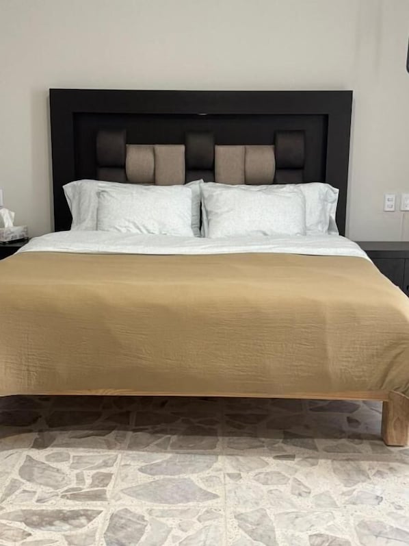 A bed with a headboard, a beige bedspread, and a stone-patterned floor.