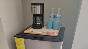 Un refrigerador de acero inoxidable con una cafetera, dos tazas azules y una pequeña bandeja con objetos.