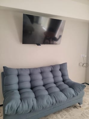 A room with a grey sofa, a mounted flat-screen TV, and a wall socket. - Suites & Lofts Olivier (Uruapan)
