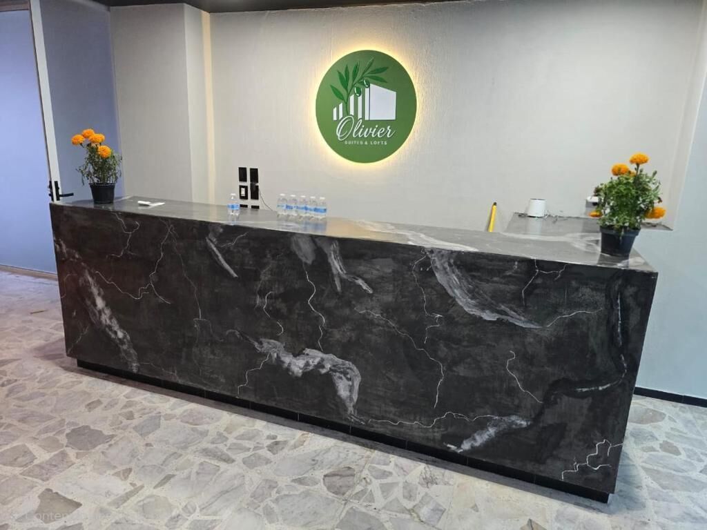 Een receptiebalie met een marmeren blad, een groen logo en twee potplanten met gele bloemen.