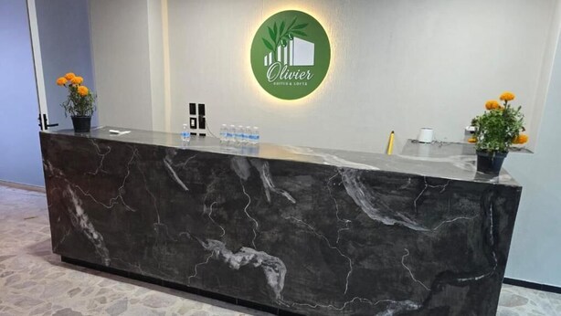 Una recepción con encimera de mármol, un logo verde y dos plantas en macetas con flores amarillas.