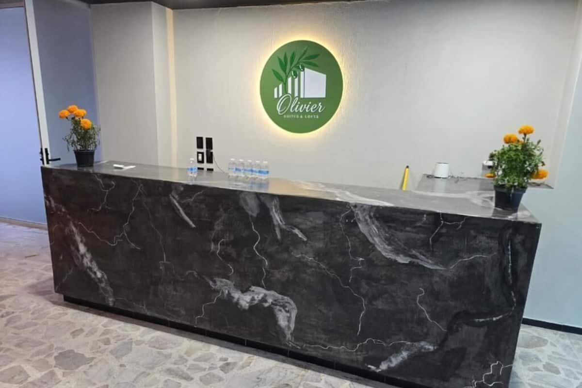 Uma mesa de recepção com tampo de mármore, um logotipo verde e duas plantas em vasos com flores amarelas.