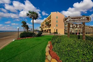 A Maravilla Resort Condominium building with a clear view of the ocean, a well-maintained lawn, and a sign indicating the address 9520. - 2 Pools, Hot Tub, Dogs Free, Right on the Beach! (Galveston)