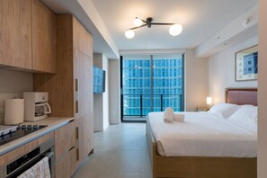 A modern hotel room with a kitchen area, a bed with white linens, a ceiling fan, and a large window with a view. - New Boutique Studio | 2 Guests | Downtown Miami (Miami)