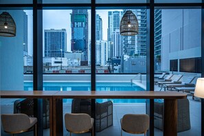 Eine Poolbar mit Stühlen und Blick auf eine Stadtkulisse durch große Fenster.