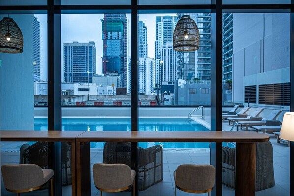 Eine Poolbar mit Stühlen und Blick auf eine Stadtkulisse durch große Fenster.