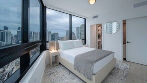 A modern bedroom with a large window, a bed, a bedside table, a walk-in closet, and a round mirror. - FREE Parking • Corner Unit • Bay & Brickell Views (Miami)