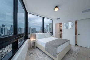 Ein modernes Schlafzimmer mit großem Fenster, einem Bett, einem Nachttisch, einem begehbaren Kleiderschrank und einem runden Spiegel.