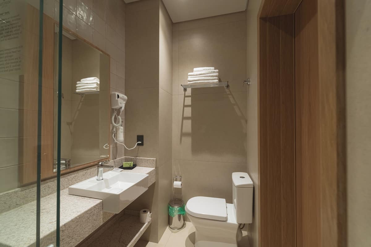 Un baño moderno con cabina de ducha de vidrio, un lavamanos blanco, inodoro y un perchero para toallas.