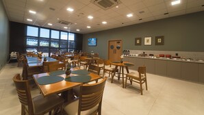 A spacious dining area with multiple tables and chairs, a kitchen counter, and large windows. - MANTRA HOTEL (Vera)