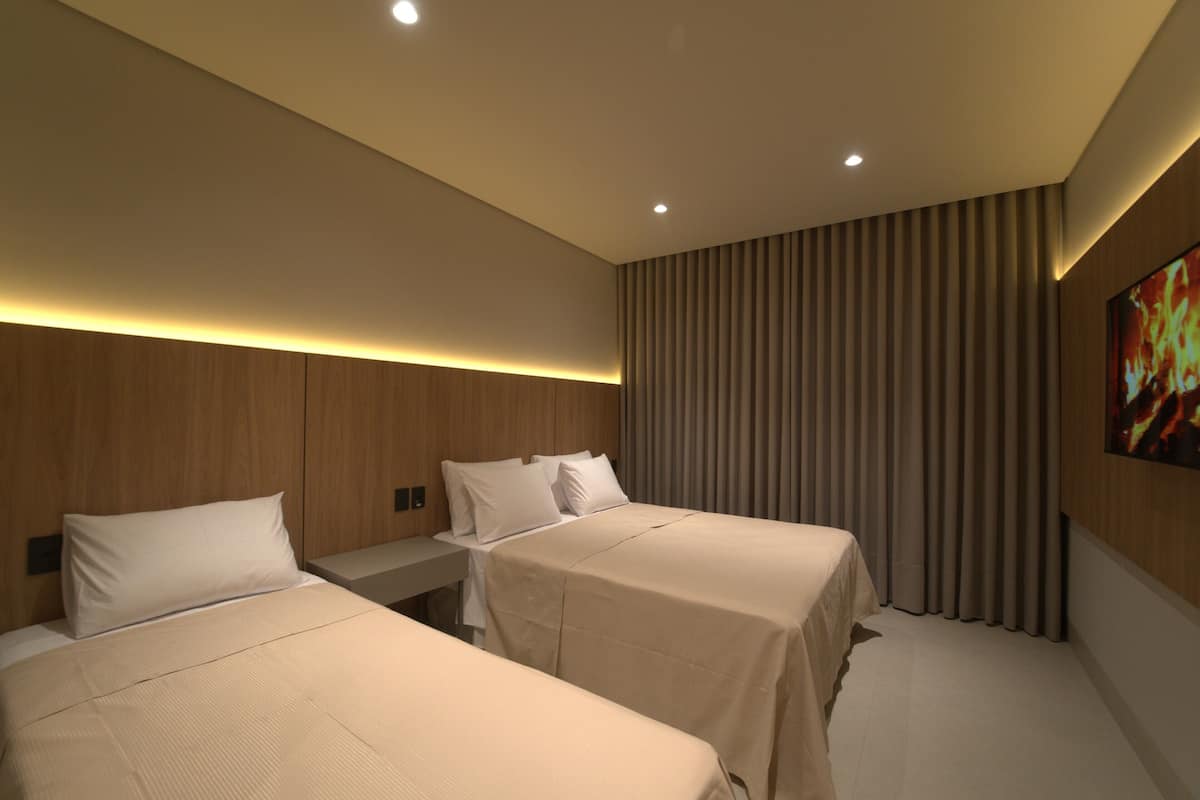 Habitación de hotel con dos camas, cabecero de madera, mesita de noche y televisor montado en la pared.