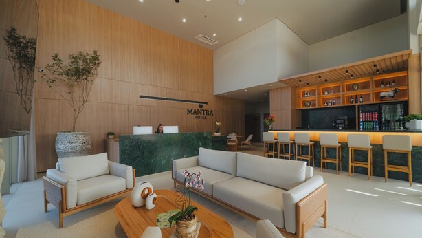 A modern hotel lobby with a reception desk, sofas, a bar area, and a large potted plant. - MANTRA HOTEL (Vera)