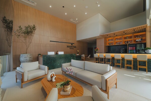 Un hall dâhĂŽtel moderne comprenant un comptoir dâaccueil, des canapĂ©s, un coin bar et une grande plante en pot.