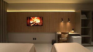 A hotel room with a TV mounted on the wall, a desk with a chair, a bed, and a wardrobe. - MANTRA HOTEL (Vera)