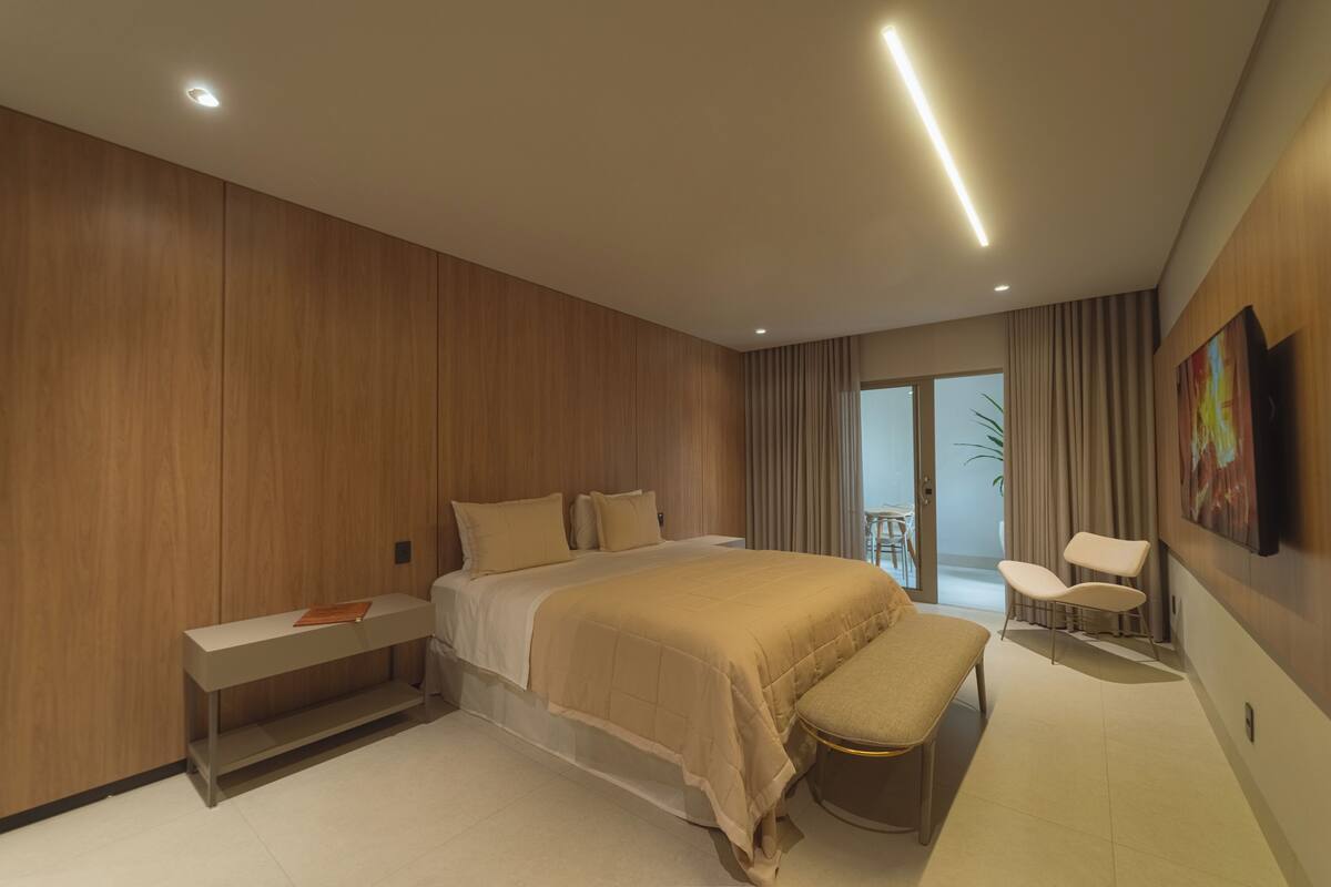 Un dormitorio moderno con una cama grande, un banco, una silla y un cuadro en la pared.
