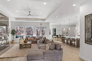 A spacious living area with a large sofa, a coffee table, and a dining area with a kitchen in the background. - Pecan Valley Oasis | Private Backyard Paradise (Hurricane)