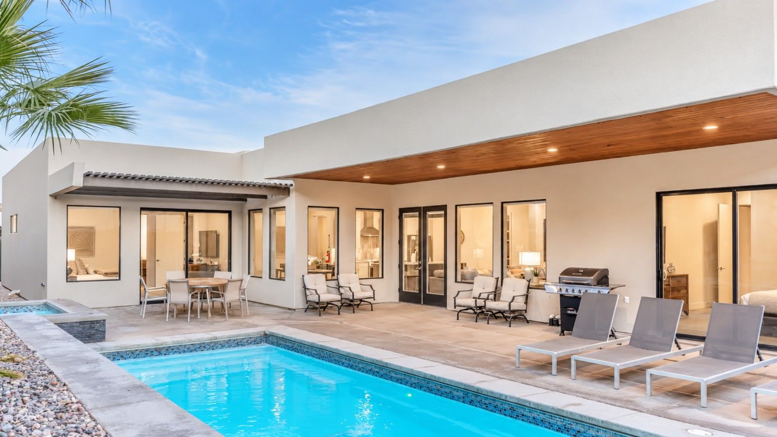 A modern outdoor pool area with a patio, seating, and a barbecue grill.