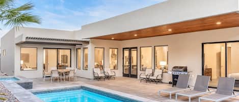 A modern outdoor pool area with a patio, seating, and a barbecue grill.