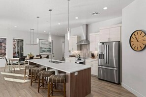 A modern kitchen with a central island, stainless steel appliances, pendant lighting, and a clock on the wall. - Pecan Valley Oasis | Private Backyard Paradise (Hurricane)
