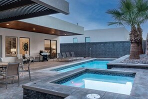 A modern outdoor pool area with lounge chairs, a barbecue, and a stone wall. - Pecan Valley Oasis | Private Backyard Paradise (Hurricane)